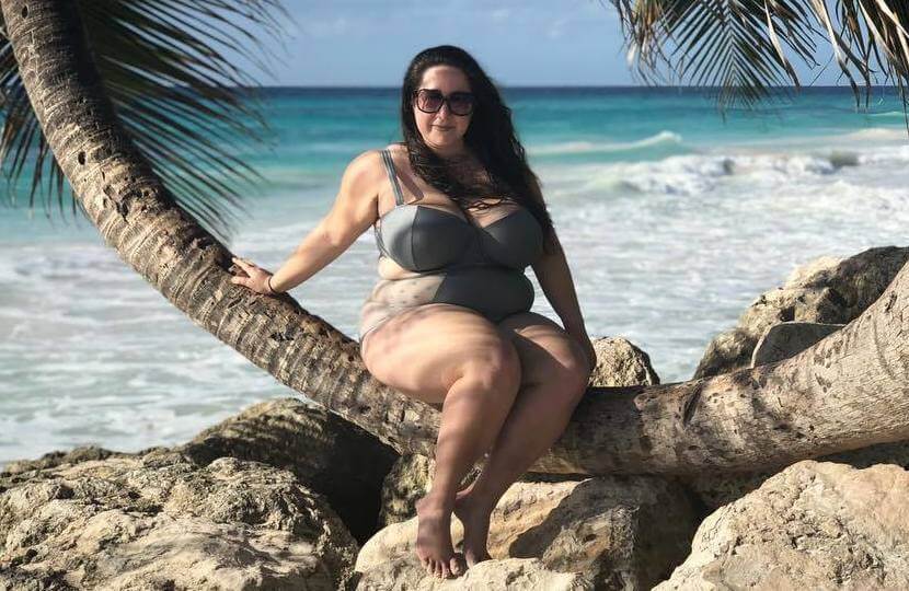 vanessa friedman wearing a one piece swimsuit and sitting on a palm tree